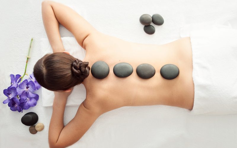 Stone treatment. Top view of beautiful young woman lying on front with spa stones on her back.  Beauty treatment concept.