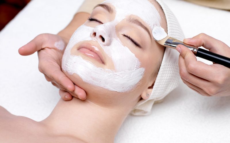 Beautiful young woman receiving facial mask at beauty salon - indoors